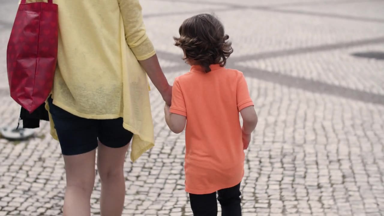 A mother and child walking hand in hand, photographed from behind.