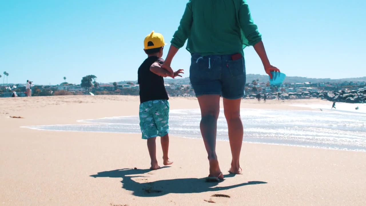 A mother and child walking together at the beach.