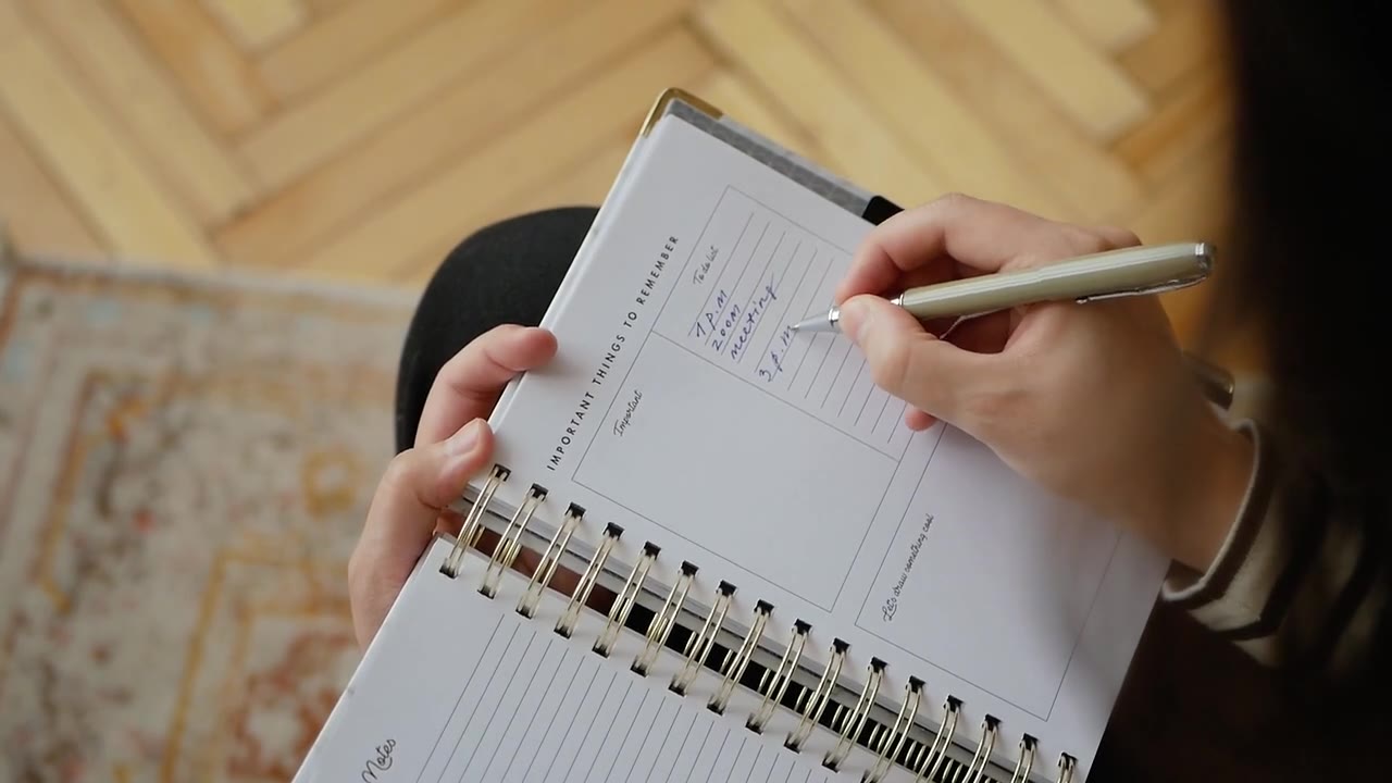 Hands writing in a planner at a table.